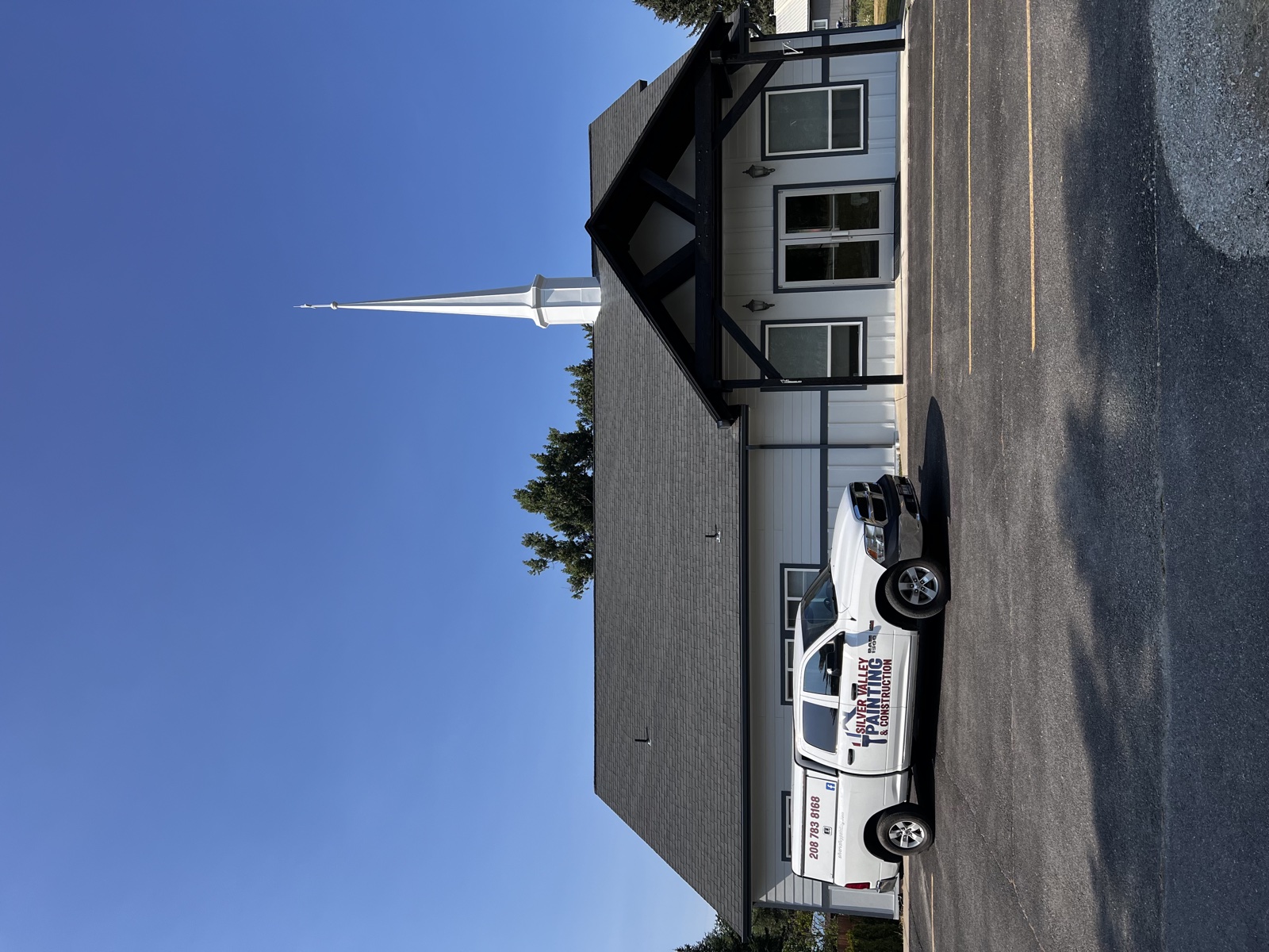 Modern church with crisp white siding, black trim, tall white steeple, and gabled entryway, with a Silver Valley work truck parked in front