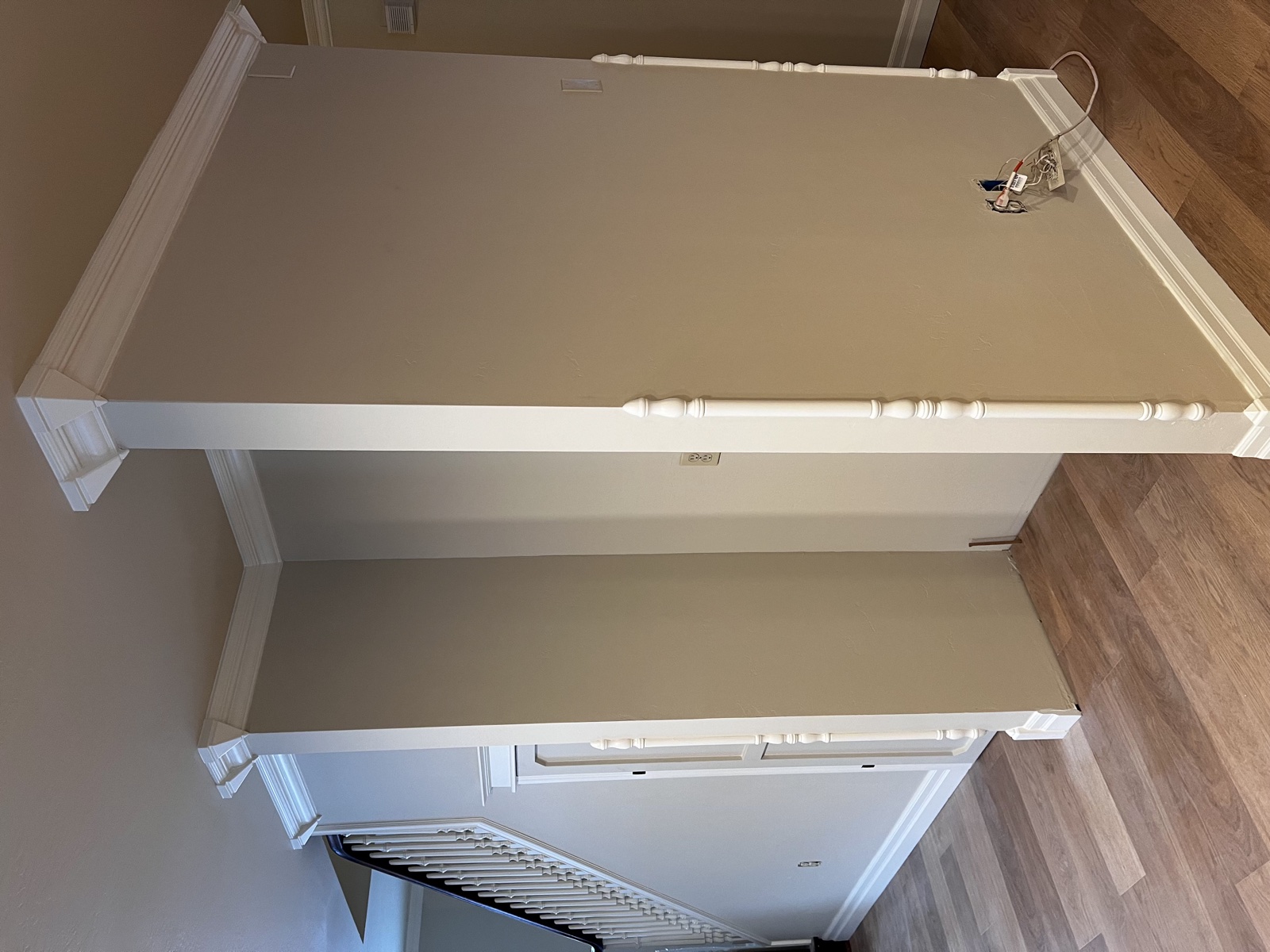 Freshly painted interior corner with crisp white wainscoting and crown molding paired with a warm tan upper wall, white stair spindles visible at right